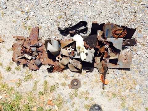1979 Ford Bronco - Rusted metal and seatbelts laid out on gravel ground.