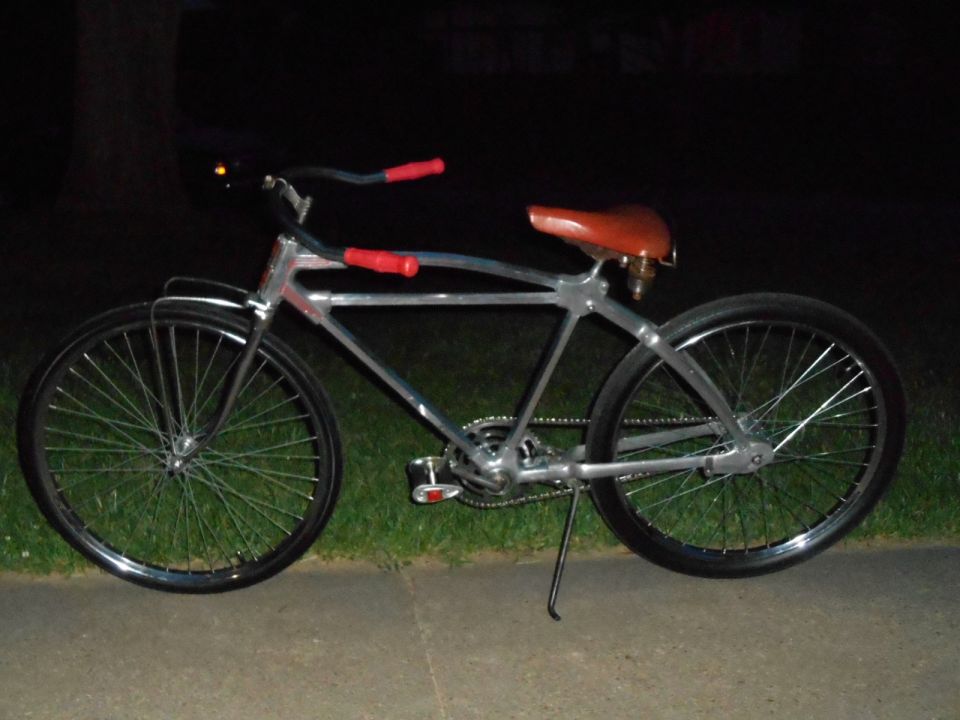 Chrome bicycle with red grips and brown seat, parked on grass