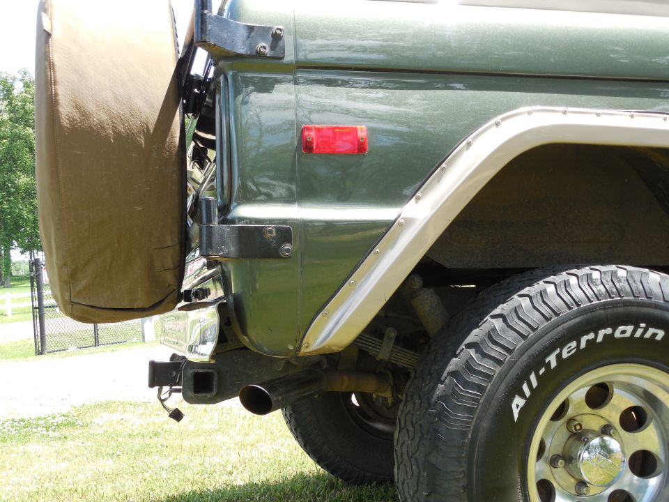 Green Bronco rear corner with tan spare tire cover, hitch receiver and All-Terrain tire