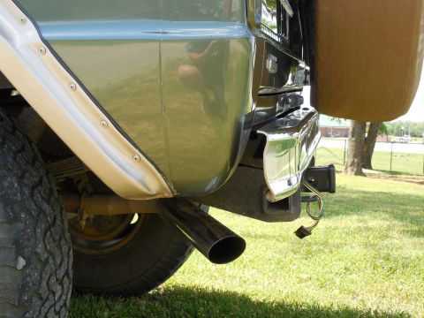 1975 Ford Bronco - Low close-up of the rear passenger corner of a green vintage Ford Bronco showing an angle-cut chrome exhaust tip exiting ahead of the bumpe…