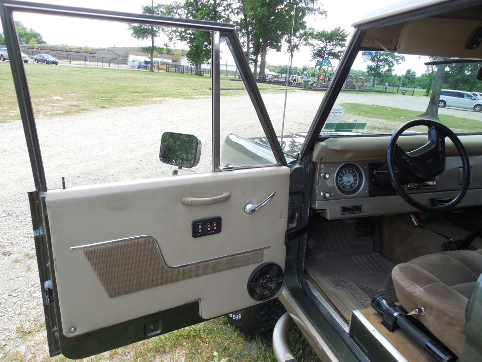 Open driver's door of a green early Ford Bronco with custom tan door panel and speaker