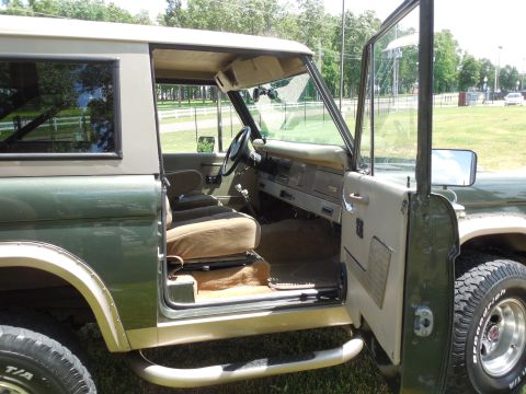1975 Ford Bronco - Passenger-side view of a green vintage Ford Bronco with the door swung open, revealing tan bucket seats and carpet, a tan painted dash, bla…