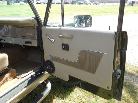 1975 Ford Bronco - Open passenger door of a green vintage Ford Bronco showing the white vinyl door panel with chrome trim strip, textured insert, chrome pull…