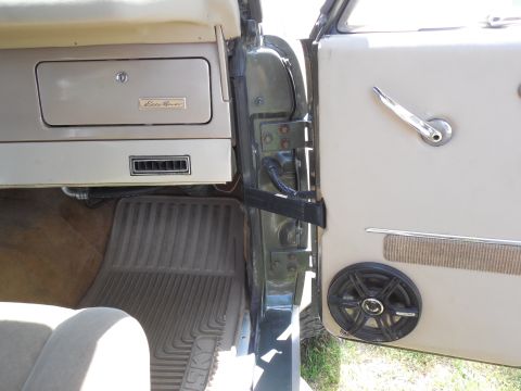 1975 Ford Bronco - Open passenger door of a green vintage Ford Bronco with an aftermarket coaxial speaker mounted low in the white vinyl door panel and a chro…