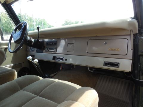 1975 Ford Bronco - Interior view across a tan early Bronco dash from the driver's side, showing a gold Eddie Bauer badge on the glovebox door, an aftermarket…