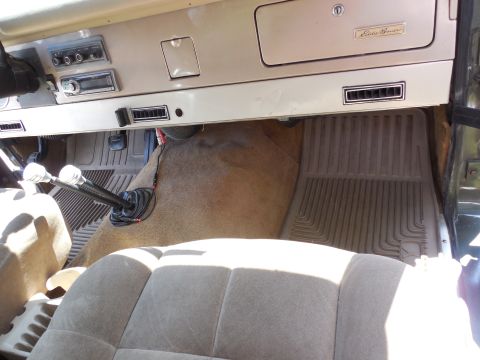 1975 Ford Bronco - Passenger-side interior of a green vintage Ford Bronco looking across the tan dash with an 'Eddie Bauer' badge on the glovebox, aftermarket…