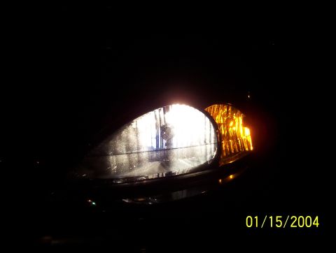 2003 Ford Taurus - The illuminated headlight assembly of a 2003 Ford Taurus is visible against a dark background.