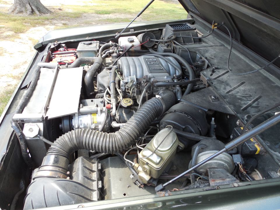 Fuel-injected Ford V8 in a green Bronco engine bay with air cleaner, A/C compressor and battery