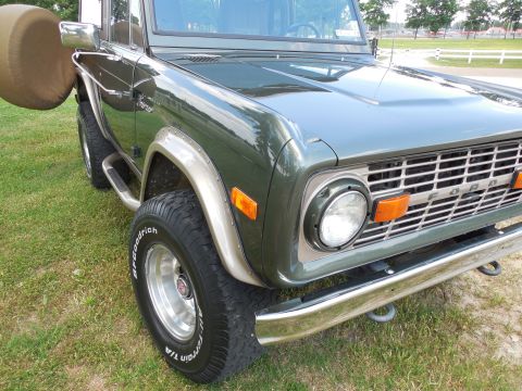 1975 Ford Bronco - Low three-quarter front shot of the passenger side of a dark green early Ford Bronco, showing the FORD-lettered grille, round headlight, am…