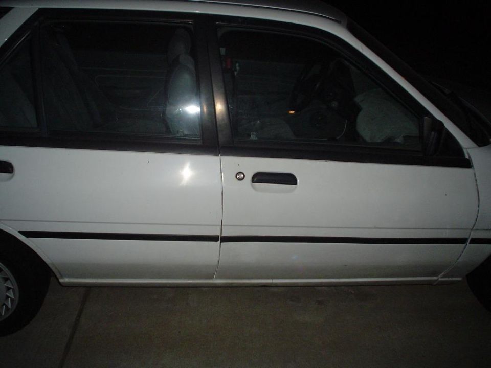 Side of a white four-door sedan with black trim, photographed at night in a driveway