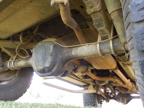 1975 Ford Bronco - Underbody shot looking up at the rear axle housing and differential of a lifted 4x4, showing leaf springs, U-bolts, shock, driveshaft, exha…