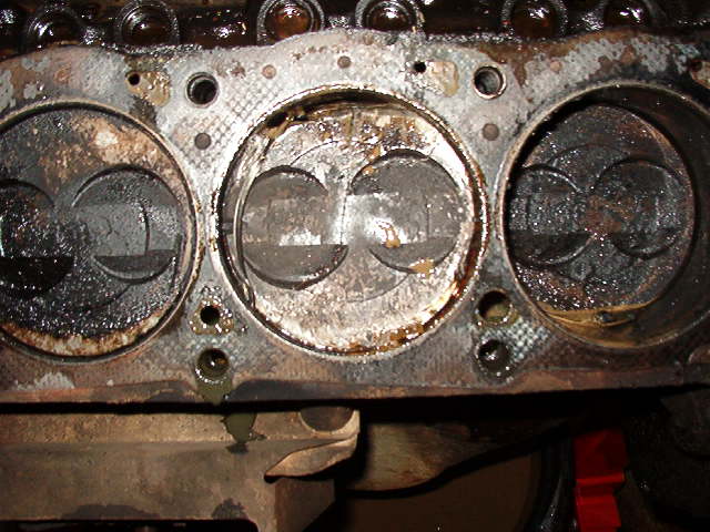 Engine block with three pistons visible, covered in oil and grime