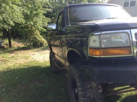 1995 Ford Bronco - A dark blue Ford Bronco with lifted suspension and off-road tires sits in a grassy area.