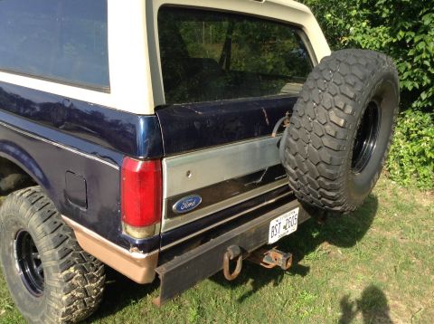 1995 Ford Bronco - Rear view of a blue and tan Ford Bronco, a spare tire mounted on the tailgate and a visible license plate.