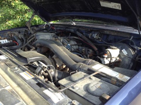 1995 Ford Bronco - The engine bay of a blue vehicle, showing the intake system and brake booster.