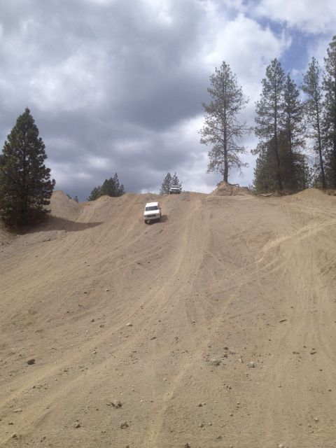 2005 Jeep Wrangler - Two white SUVs navigate a steep sandy incline on an off-road trail under a dramatic cloudy sky.