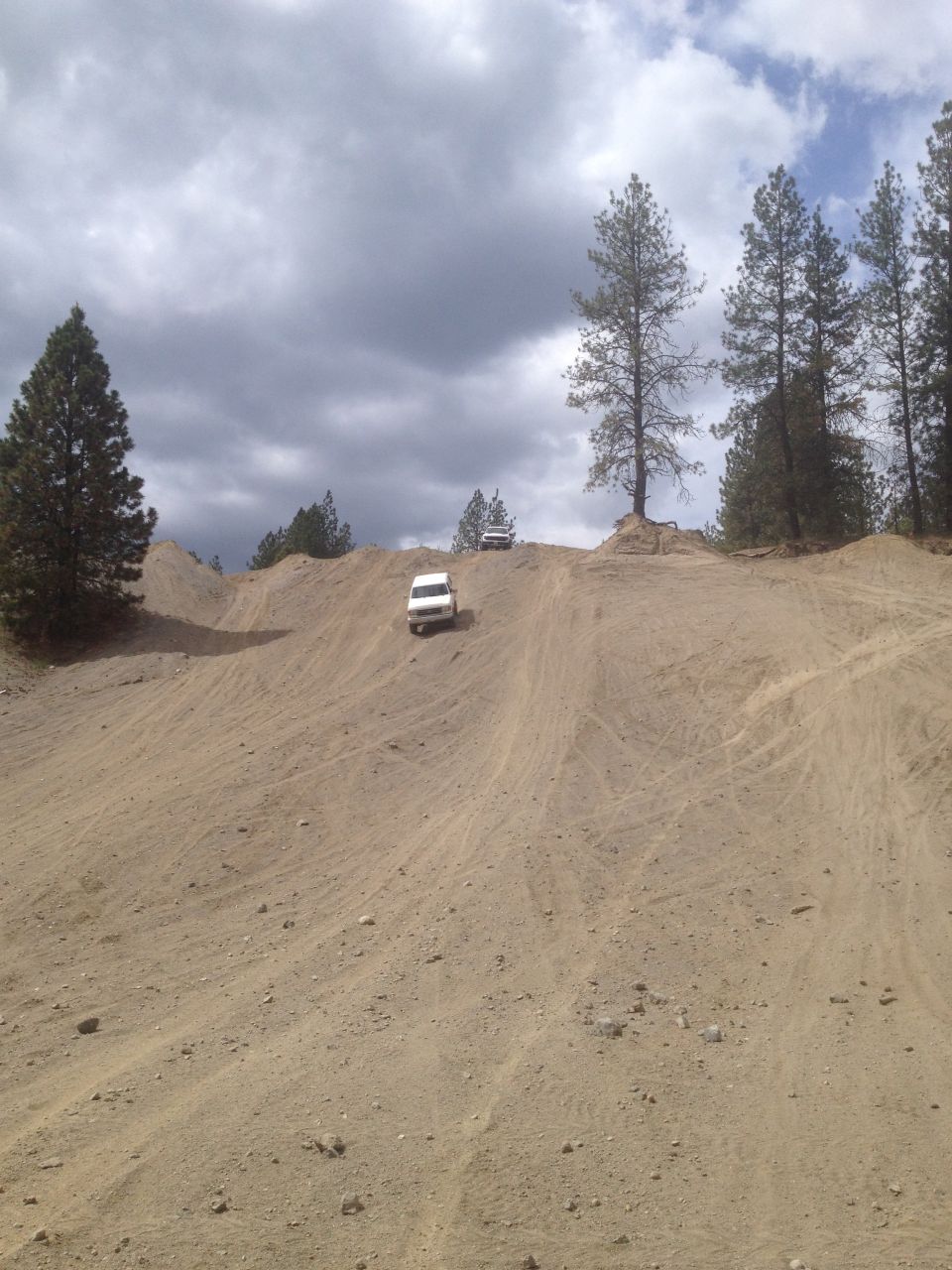 Two white SUVs on a sandy hill under a cloudy sky