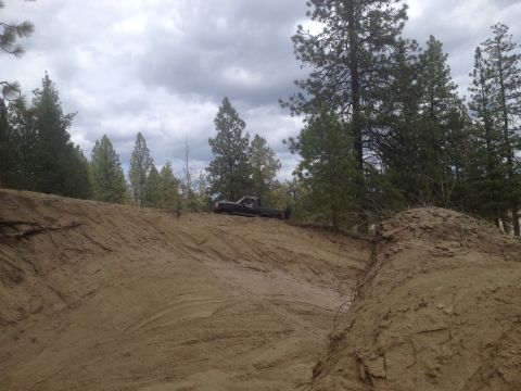 2005 Jeep Wrangler - A black pickup truck is parked on a dirt embankment under a cloudy sky, surrounded by trees.