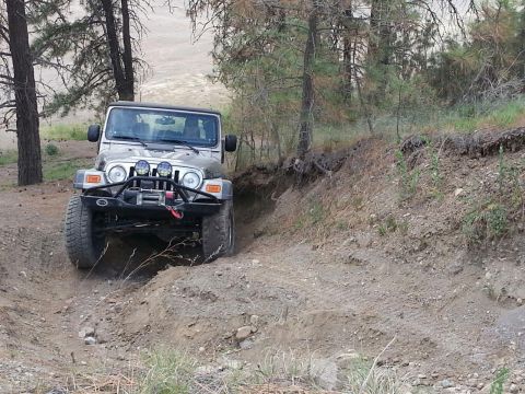 2005 Jeep Wrangler - A silver Jeep Wrangler navigates a steep, dry dirt trail surrounded by trees.