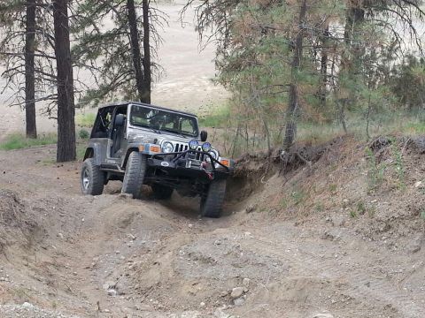 2005 Jeep Wrangler - A silver 2005 Jeep Wrangler navigates a dirt path through a wooded area.