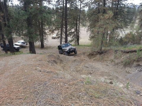 2005 Jeep Wrangler - A 2005 Jeep Wrangler navigates a steep dirt trail in a wooded area with other vehicles nearby.
