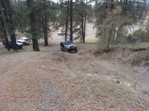 2005 Jeep Wrangler - A silver Jeep Wrangler navigates a steep dirt trail in a wooded area, with other vehicles in the background.
