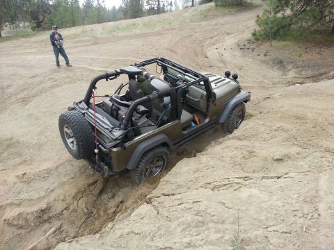 2005 Jeep Wrangler - A brown Jeep Wrangler navigates a challenging dirt path with a person standing in the background.