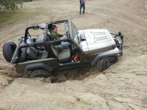 2005 Jeep Wrangler - A brown 2005 Jeep Wrangler Rubicon is stuck in the sand with its front wheel deep in a rut.