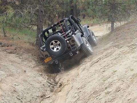 2005 Jeep Wrangler - A Jeep Wrangler navigates a challenging off-road trail, kicking up dust as it ascends a steep incline.