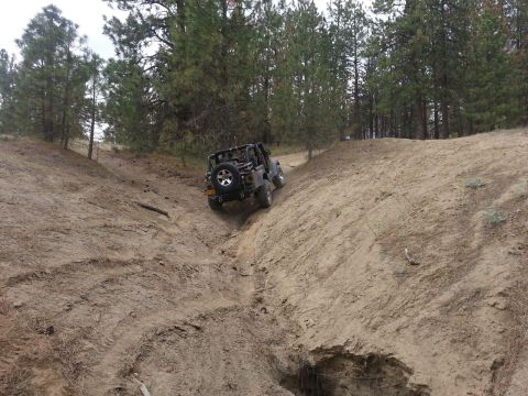 2005 Jeep Wrangler - A Jeep Wrangler navigates a challenging off-road trail, descending into a narrow dirt gully.