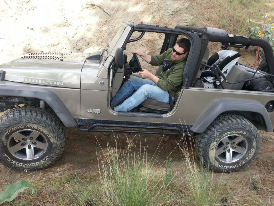 Tan 2005 Jeep Wrangler Rubicon with a man driving, seen from the side