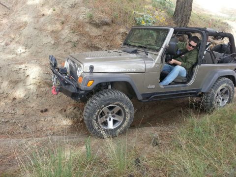 2005 Jeep Wrangler - A tan 2005 Jeep Wrangler navigates an off-road trail with a driver looking at their phone.