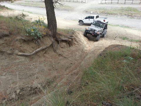 2005 Jeep Wrangler - A silver 2005 Jeep Wrangler navigates an off-road trail, while a white pickup truck waits on higher ground.