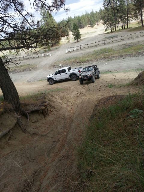 2005 Jeep Wrangler - Two off-road vehicles parked on a dirt track in a wooded, hilly area.