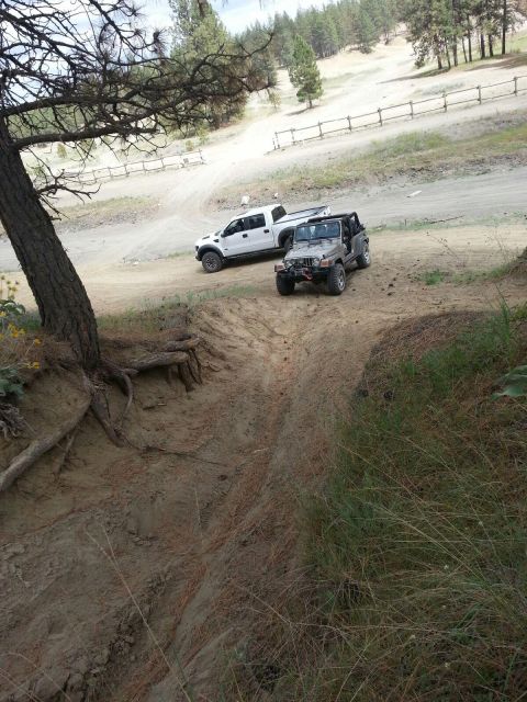 2005 Jeep Wrangler - Two off-road vehicles, a Jeep Wrangler and a pickup truck, are parked on a dirt track in a wooded area.
