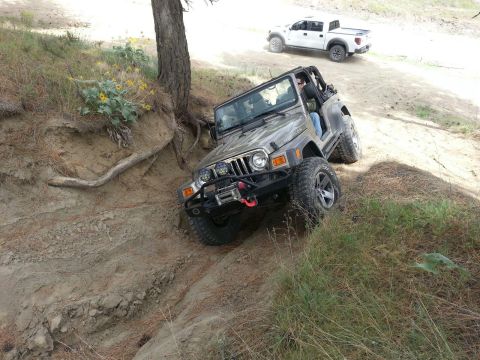 2005 Jeep Wrangler - A silver 2005 Jeep Wrangler navigates a challenging off-road trail, while a white pickup truck follows behind on a dusty path.