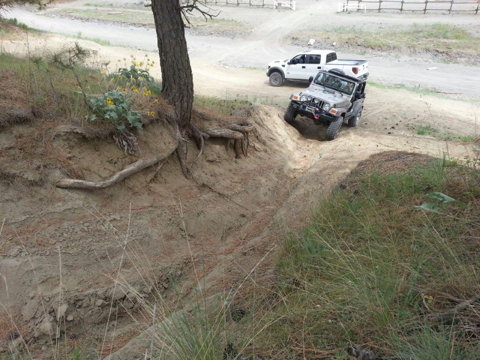 Silver 2005 Jeep Wrangler driving down a dirt embankment with a white pickup truck behind it