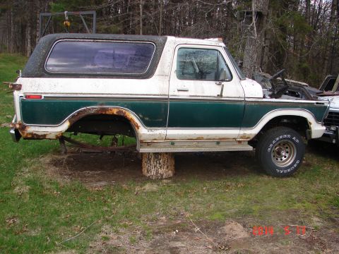 1978 Ford Bronco - A 1978 Ford Bronco sits on logs, missing its rear wheels and showing signs of rust and disrepair.