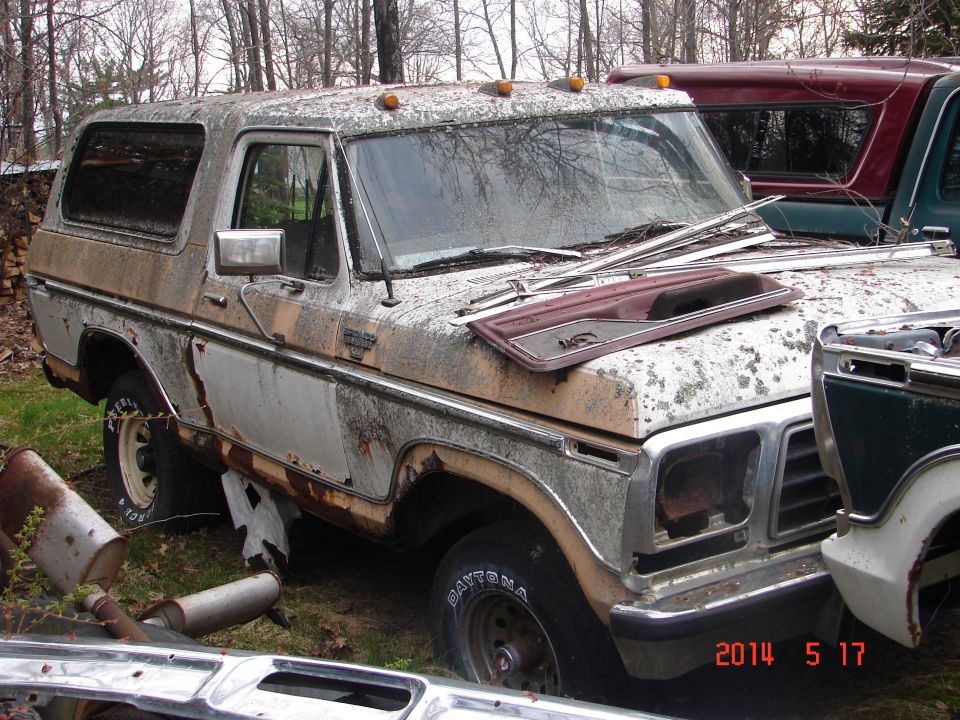 Old Ford Bronco with rust and peeling paint, parked outside with other vehicles