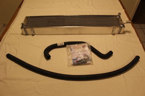 2003 Ford Crown Victoria - polished aluminum heat exchanger lies on a cloth with two curved black hoses and a bag of mounting hardware.
