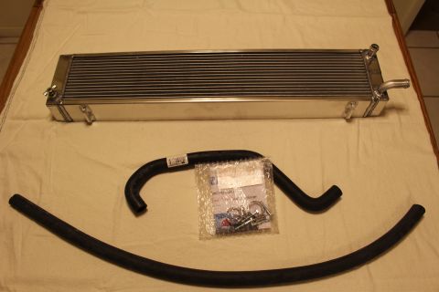 2003 Ford Crown Victoria - aluminum cooler core sits on a cloth alongside two black rubber hoses and a sealed bag of fittings.