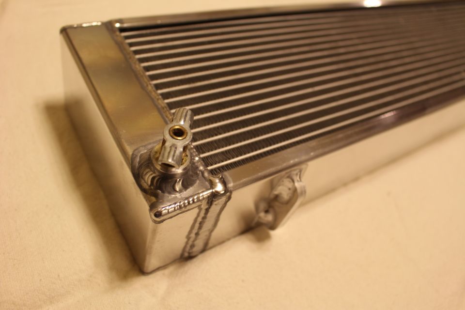 Close-up of a polished aluminum heat exchanger corner with a brass drain fitting and welds