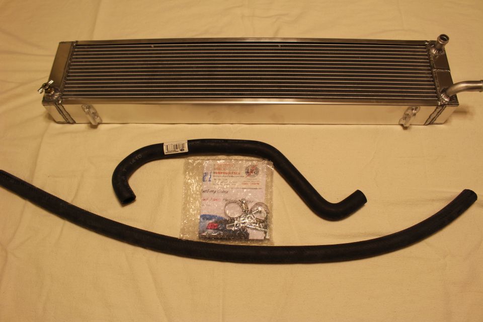Aluminum heat exchanger laid out with two black hoses and a bagged hardware kit on cloth