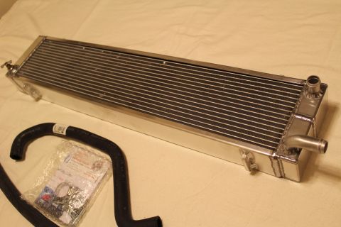 2003 Ford Crown Victoria - polished aluminum heat exchanger sits at an angle on tan cloth next to a curved black hose and a bagged hardware kit.