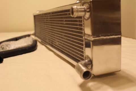 2003 Ford Crown Victoria - Low-angle close-up of an aluminum heat exchanger showing its fin core, welded end tank and a protruding hose barb.