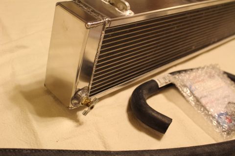 2003 Ford Crown Victoria - Close-up of an aluminum heat exchanger end tank with a brass drain fitting beside a bagged black hose.