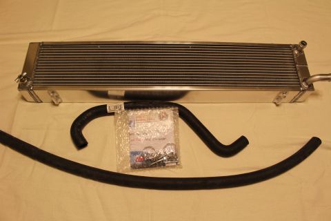 2003 Ford Crown Victoria - aluminum heat exchanger with mounting tabs is laid above a curved black hose and a clear bag of clamps.
