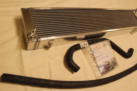 2003 Ford Crown Victoria - aluminum heat exchanger sits at an angle beside a black coolant hose and a bagged hardware kit on tan cloth.