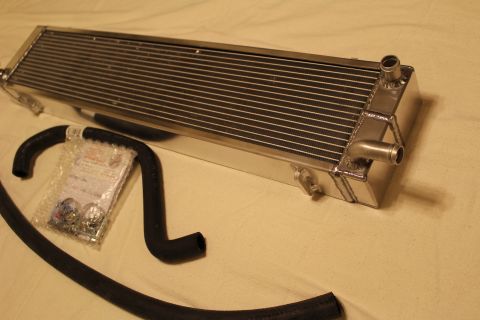 2003 Ford Crown Victoria - aluminum heat exchanger with twin barbed fittings rests beside black hoses and a sealed bag of hardware.
