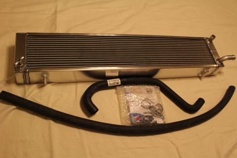 2003 Ford Crown Victoria - aluminum heat exchanger with a mounting tab lies above a black hose and a clear bag of clamps and hardware.